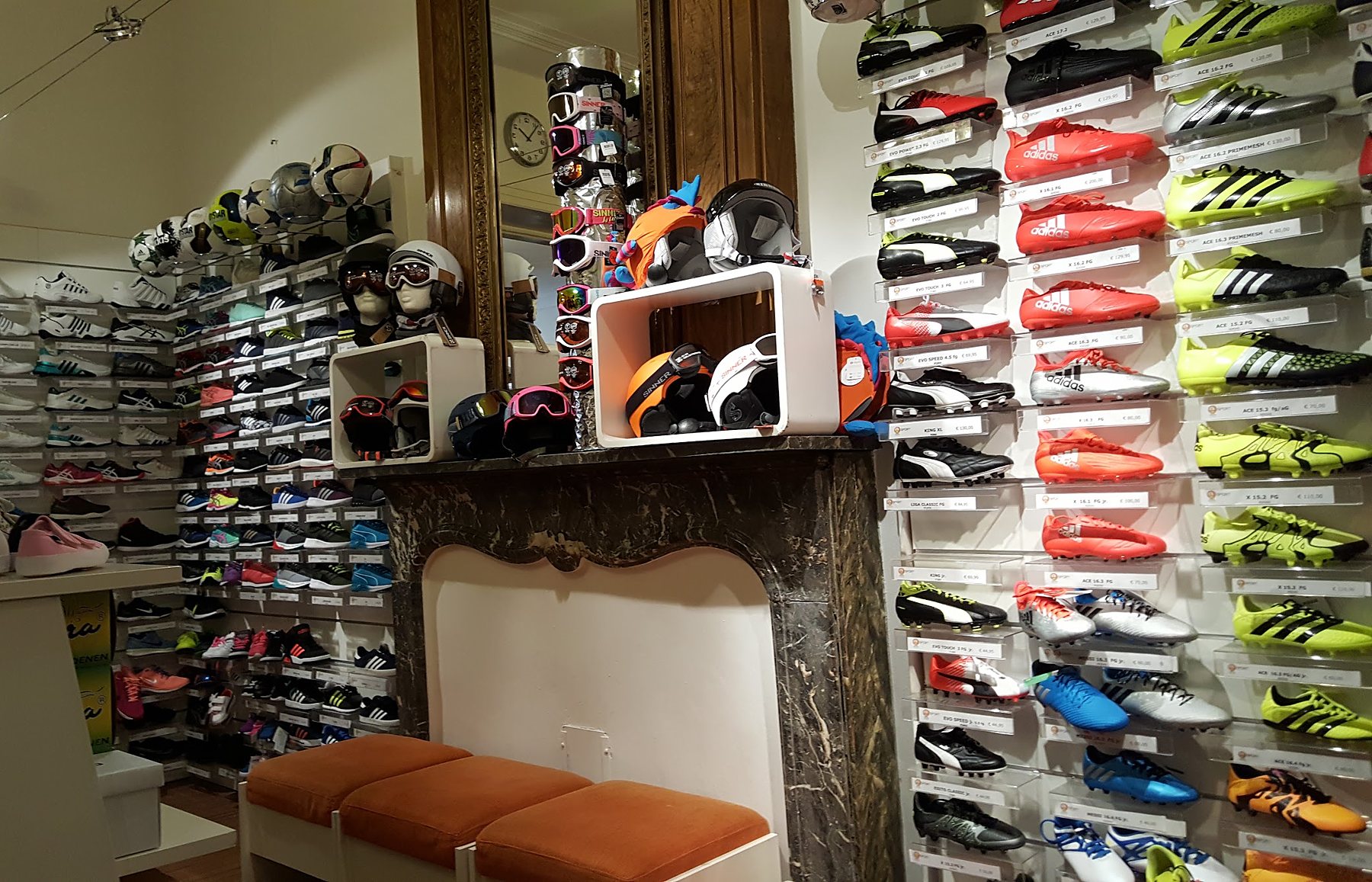 De winkel van binnen: marmeren schouw met vergulde spiegel, oranje krukjes om te passen en een wand vol voetbalschoenen